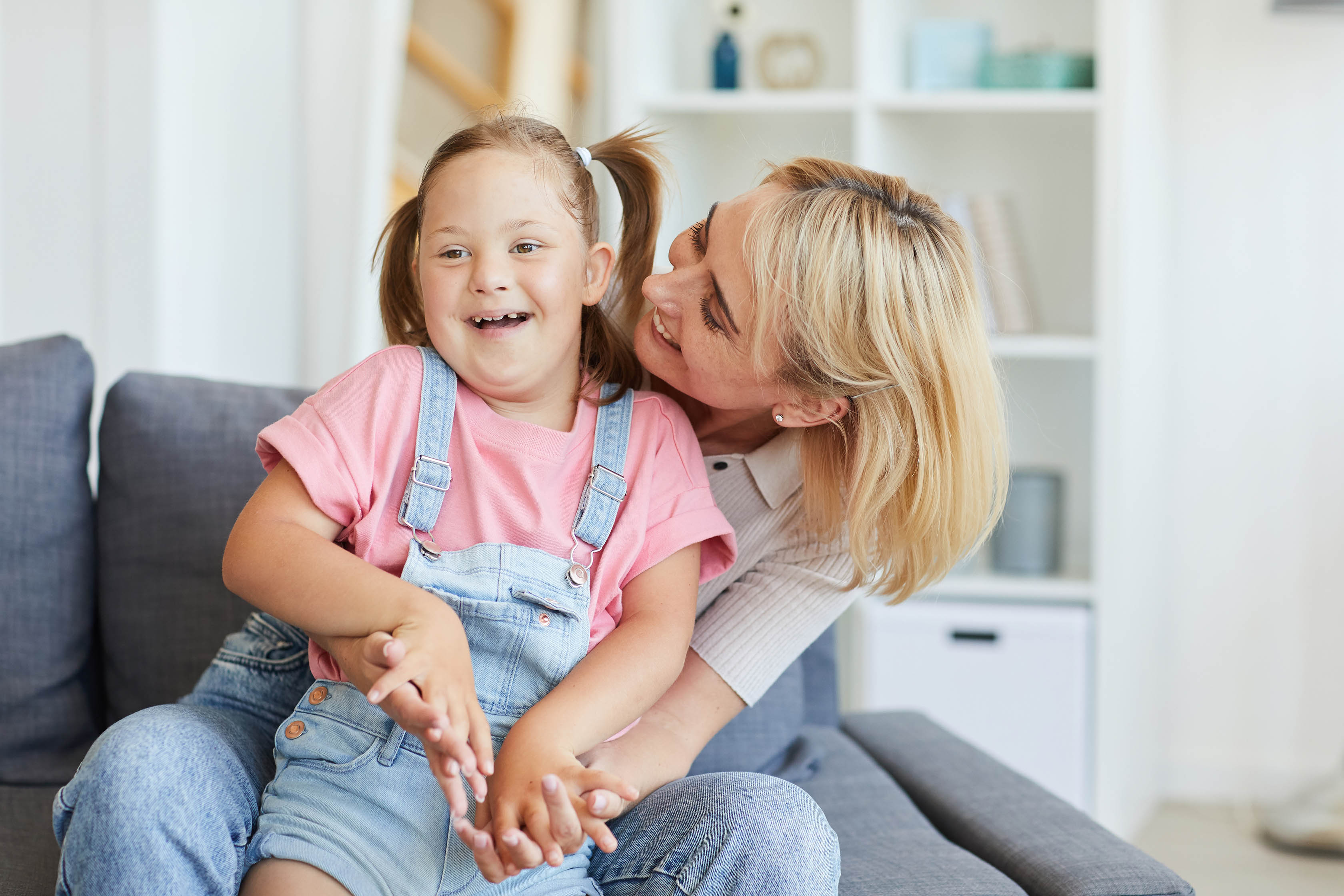 Woman hugging smiling girl on sofa indoors.