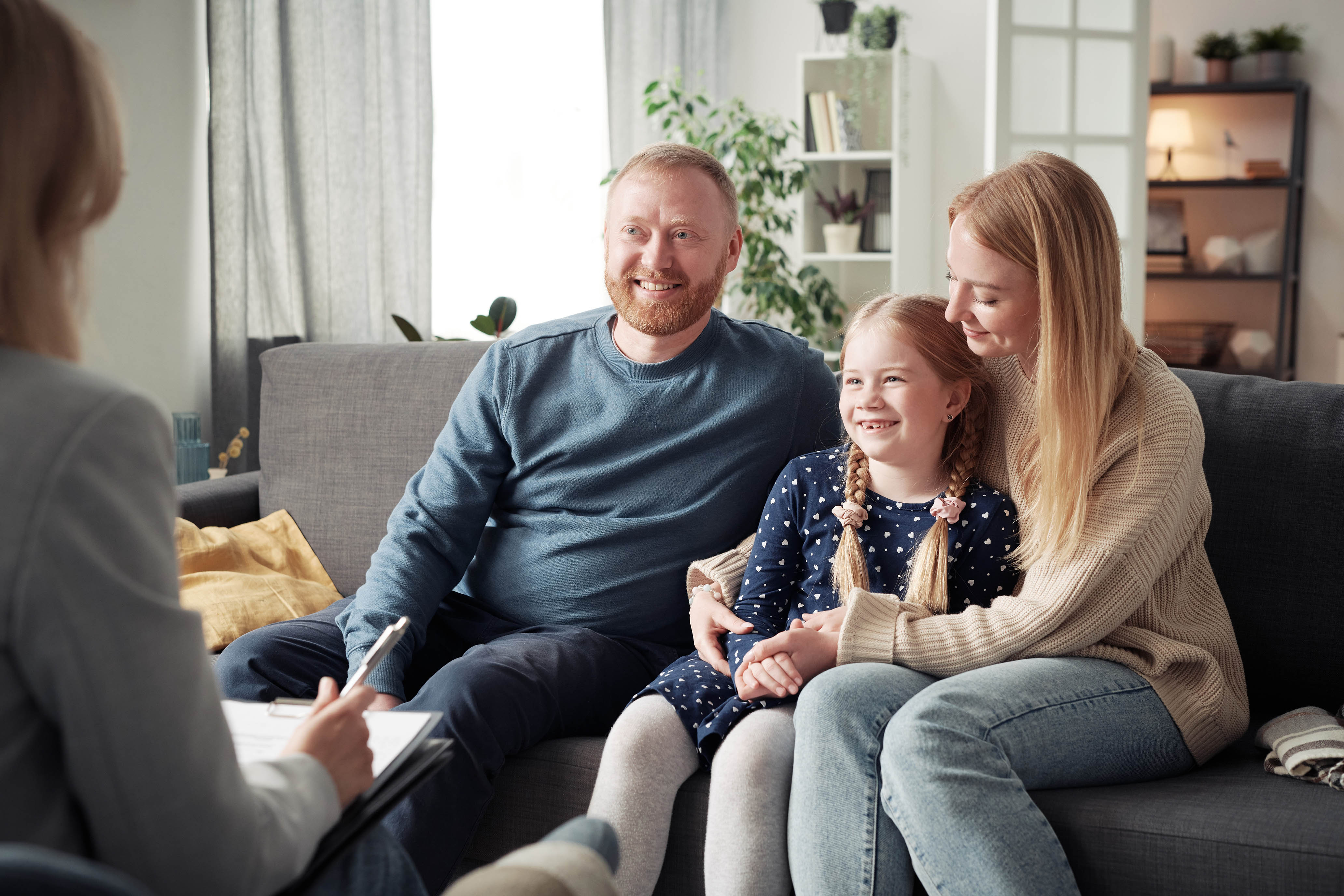 Family sitting on a sofa, smiling, during a counseling session.