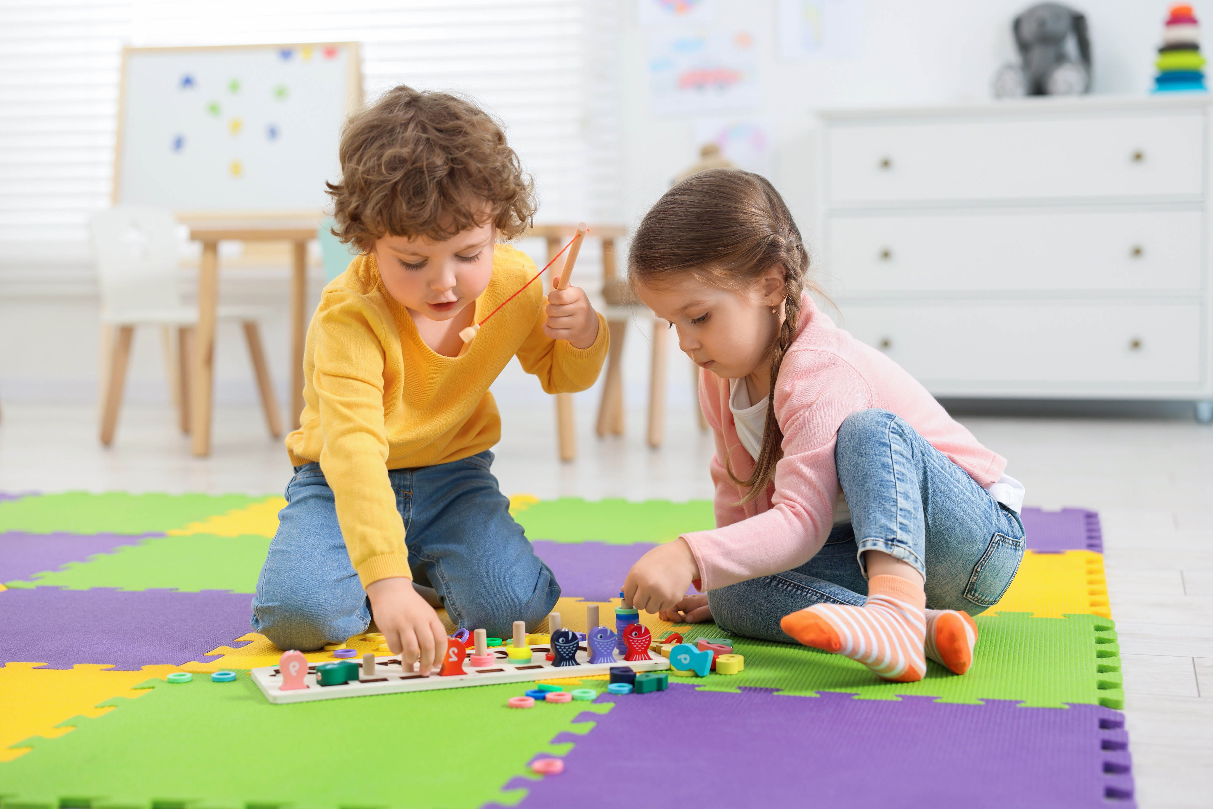 Children playing with colorful blocks on a soft mat indoors.