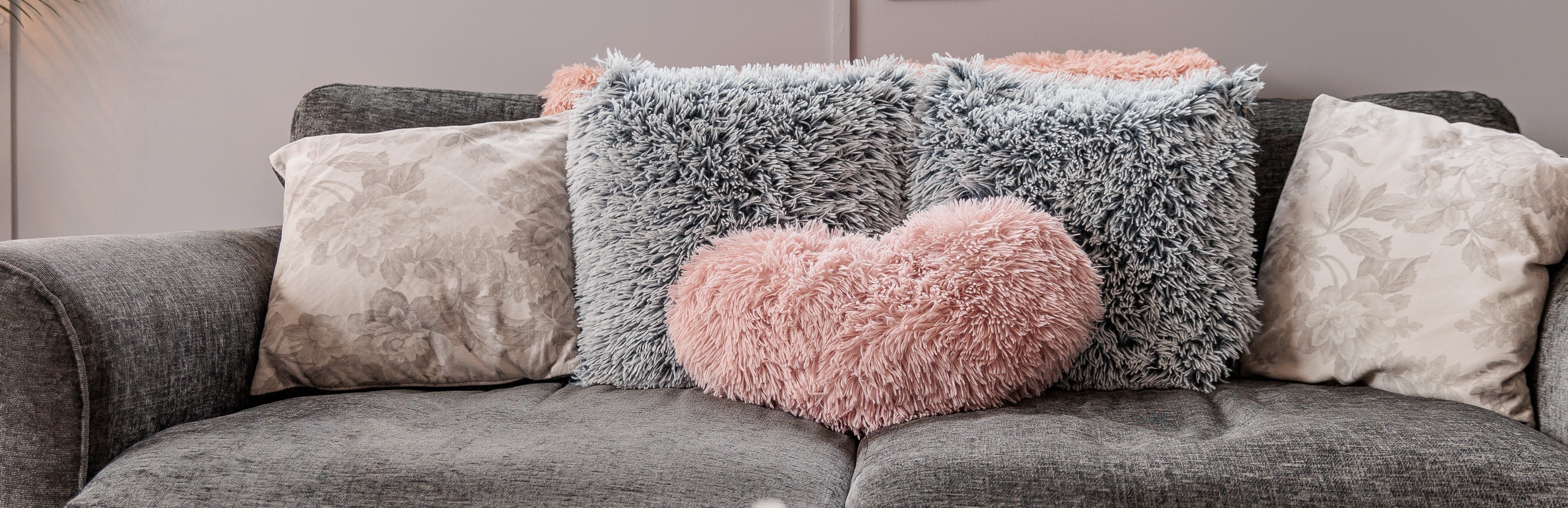 Grey sofa with fluffy cushions, one pink heart-shaped.