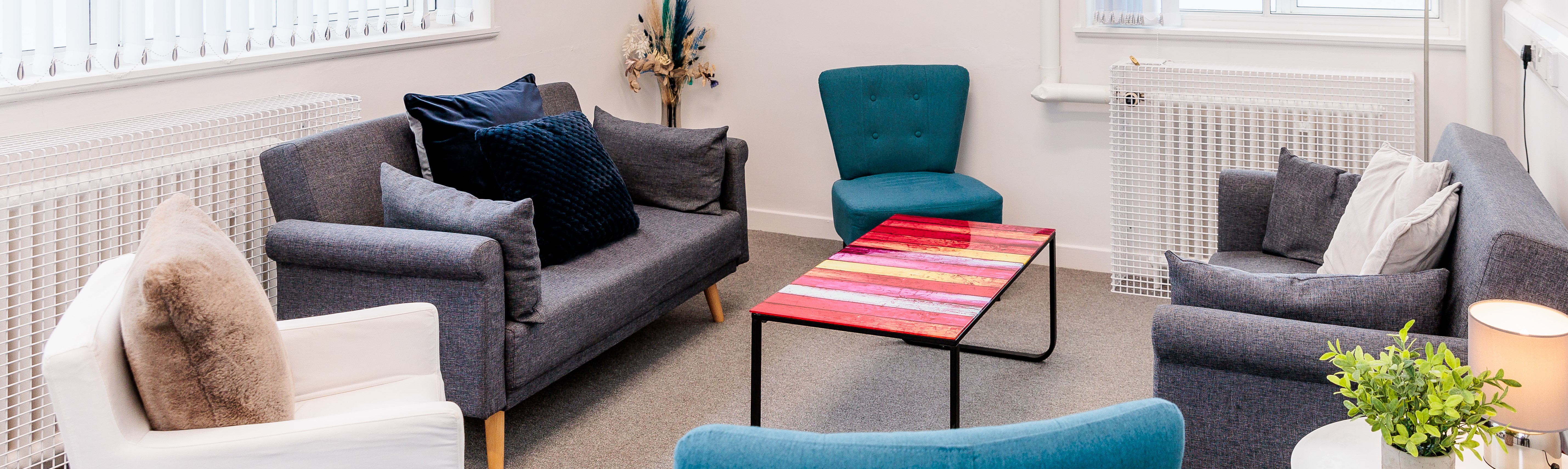 Cozy living room with sofas, a turquoise chair, and a colourful coffee table.