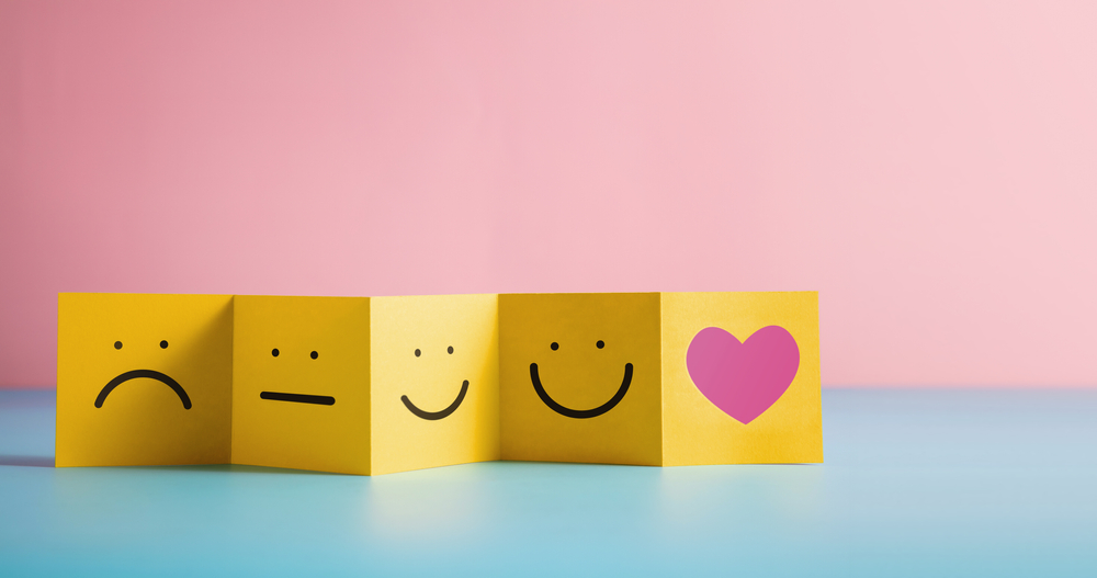 Yellow sticky notes with sad, neutral, happy faces, and a pink heart on a pink background.