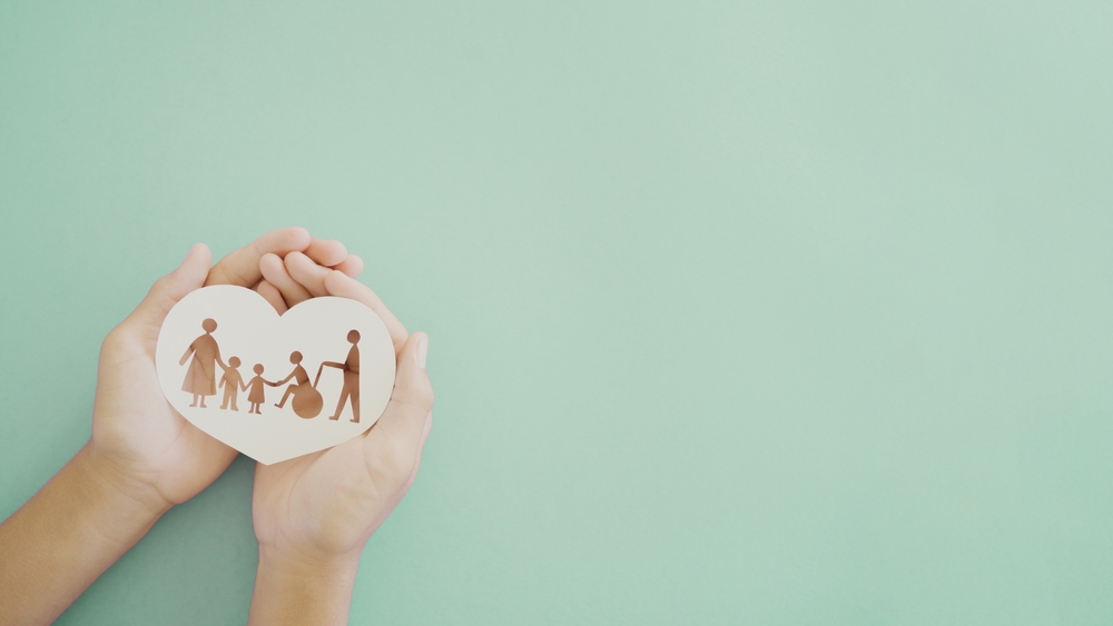 Hands holding a paper cut-out of a family on a light teal background.