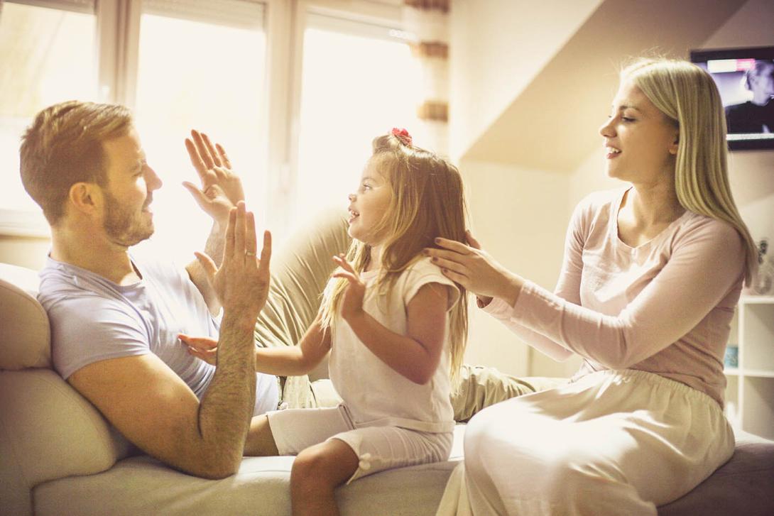 Family smiling and playing on a sofa in a sunlit room.