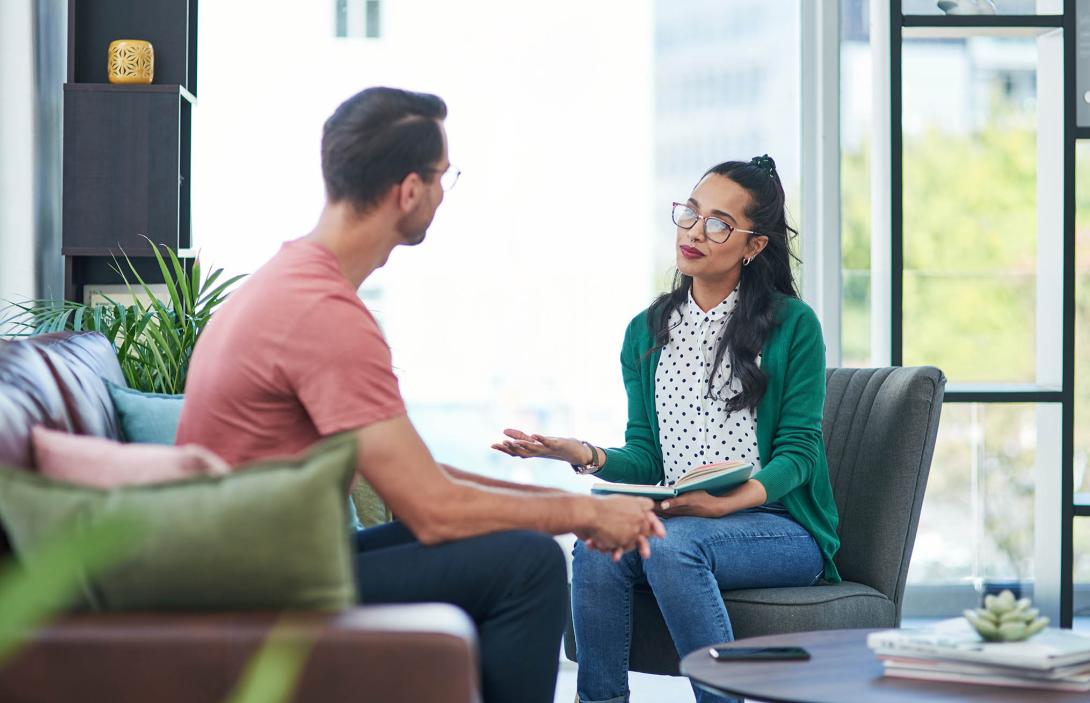 Two people engaged in conversation on a sofa in a modern office setting.